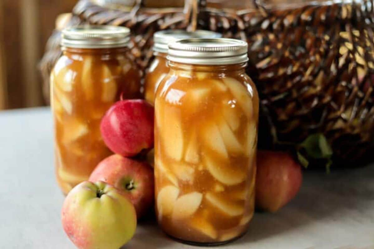 Apple pie filling in three glass jars with ripe apples around.