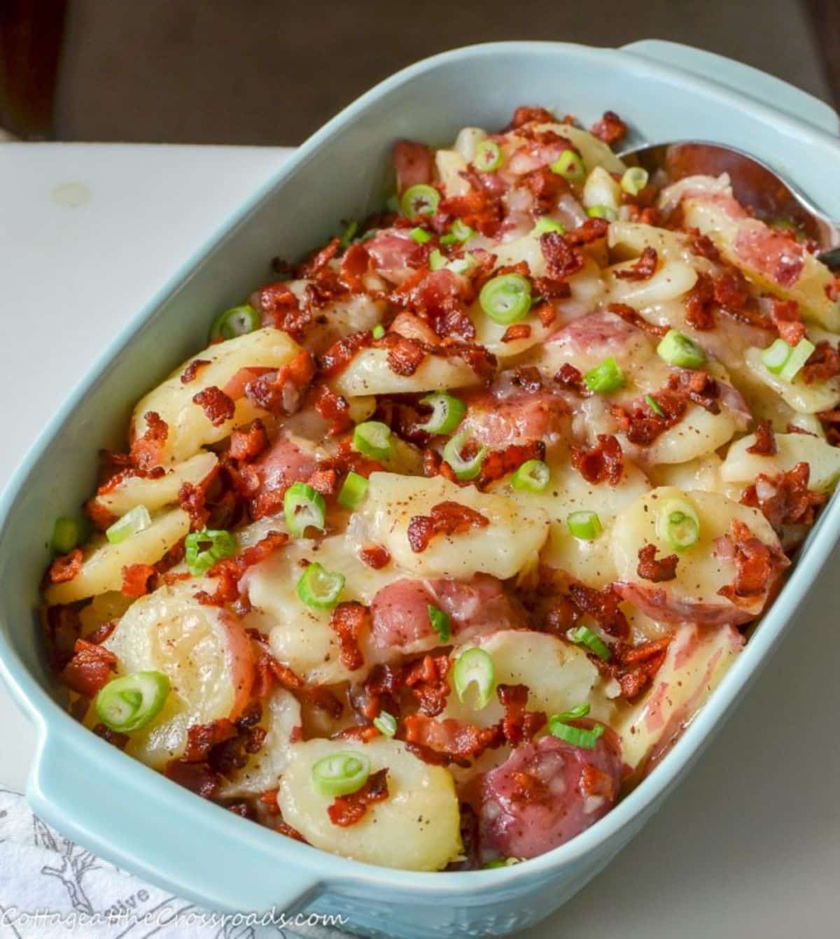 Warm german potato salad with bacon in a blue casserole.