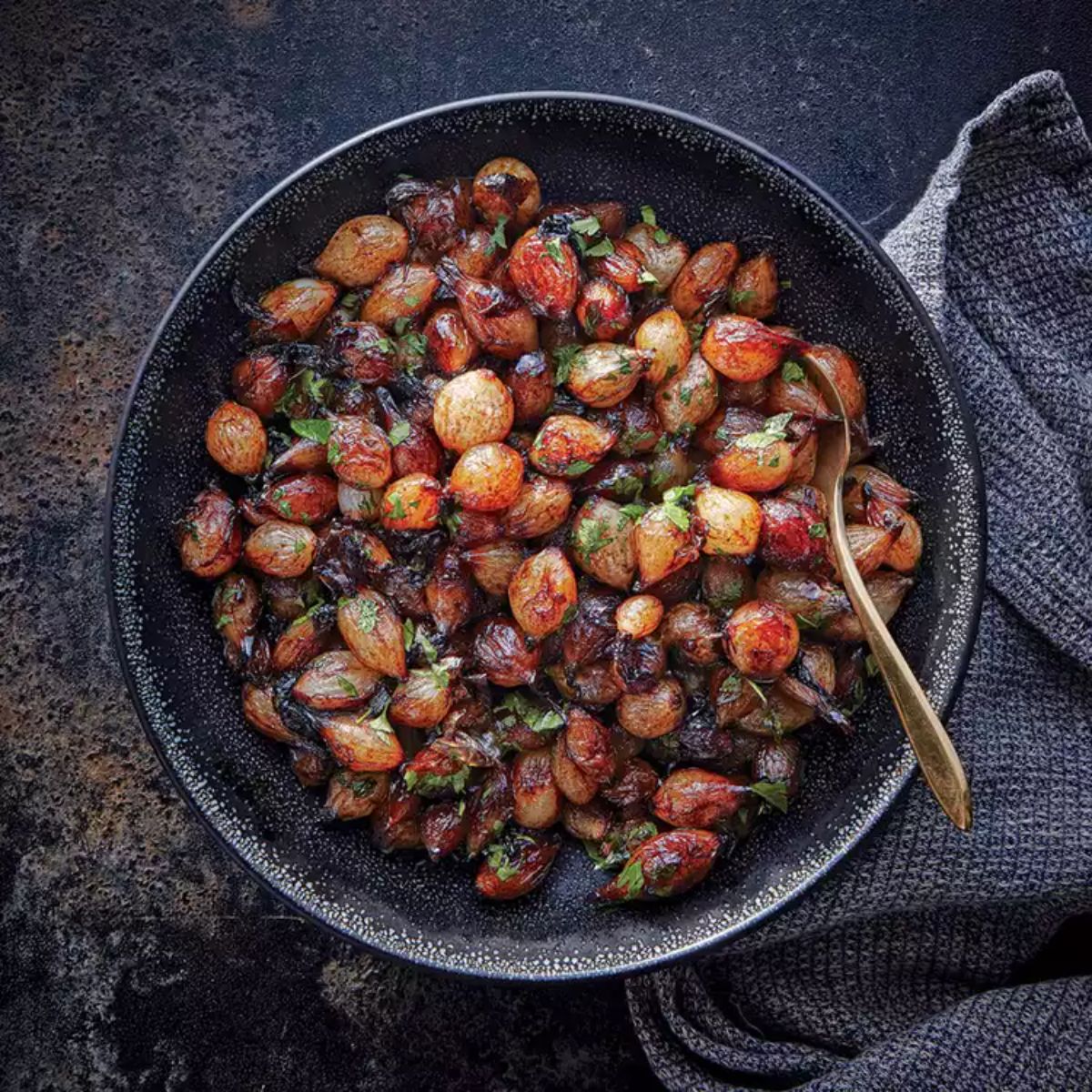 Balsamic-glazed pearl onions in a black skillet with a spoon.