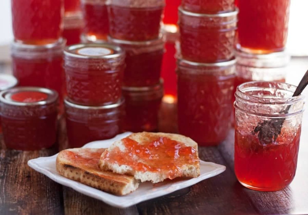 Quince jelly in glass jars and on two slices of bread on a white plate.