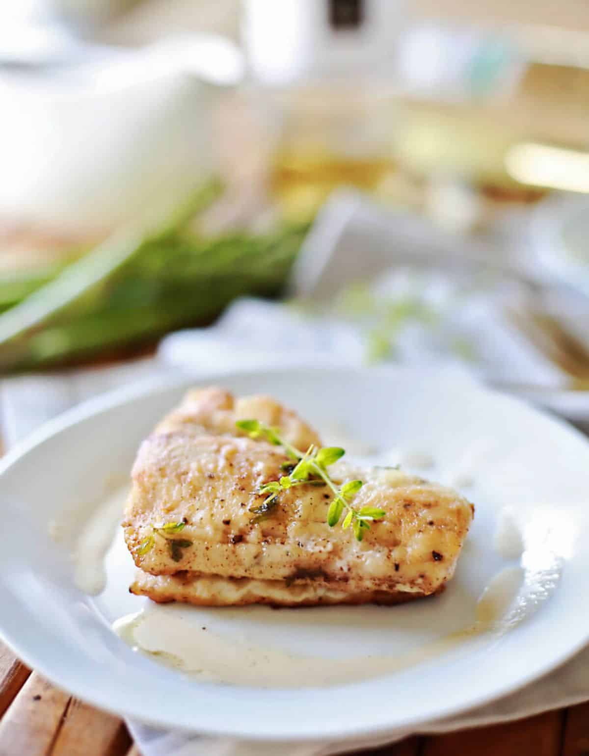 A piece of haddock in butter wine sauce on a white plate.