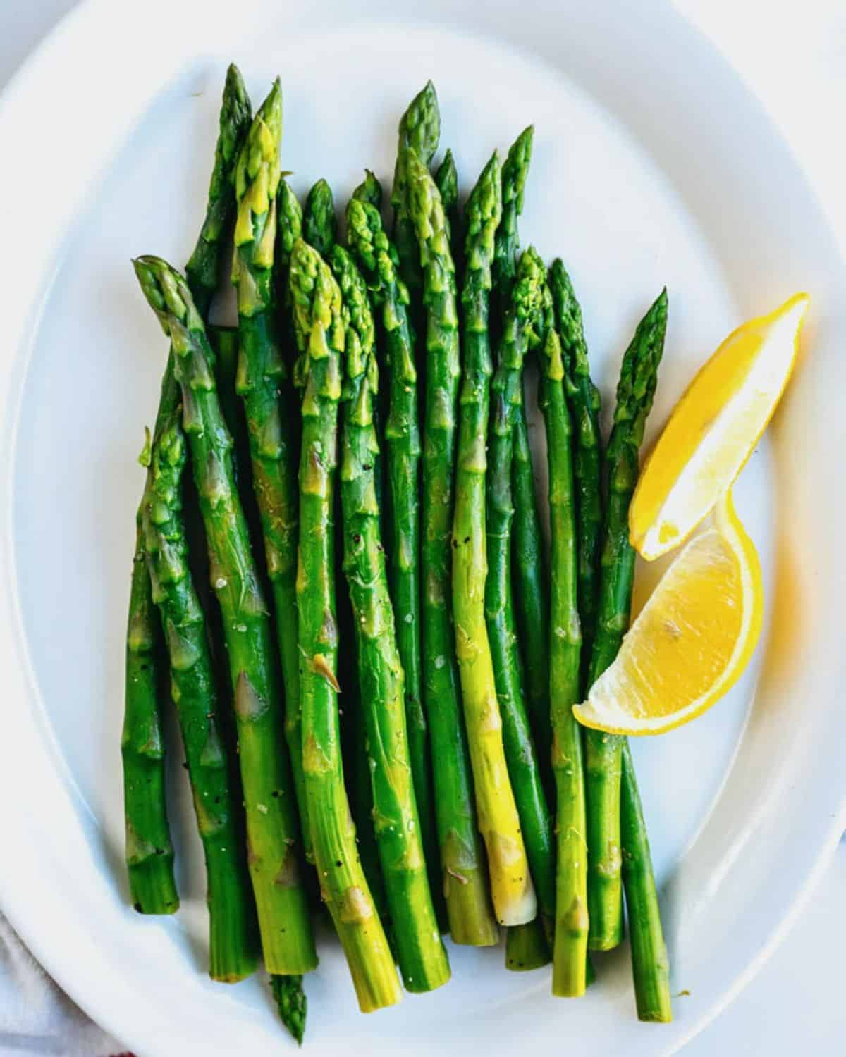 Boiled asparagus wtih slices of lemon on a white plate.