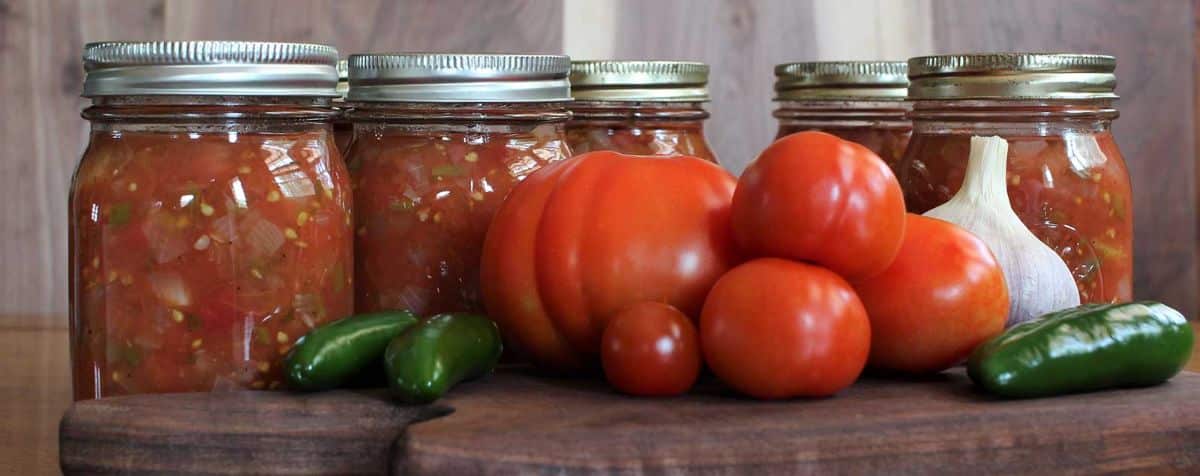 Canned kidney bean chili with ground beef in glass jars with veggies on a wooden cutting board.