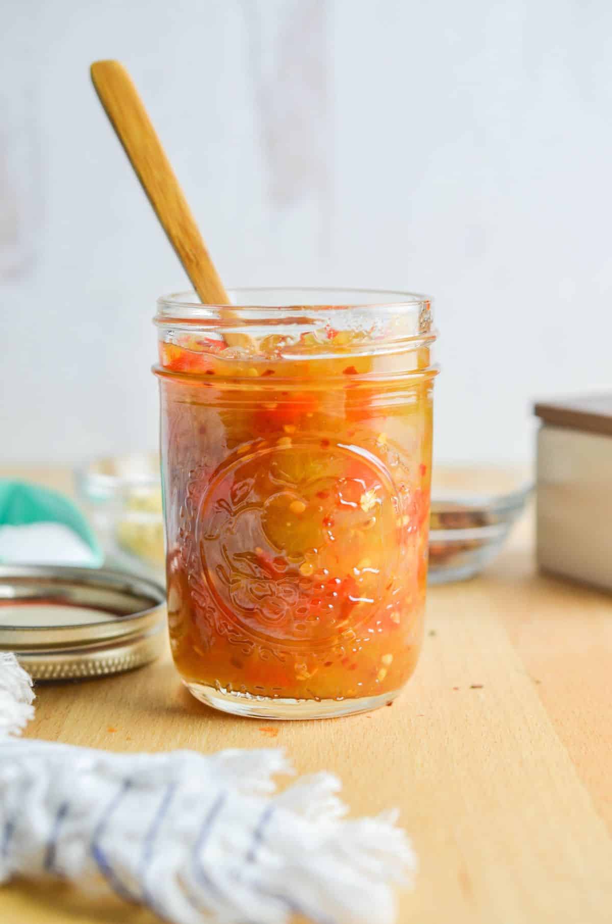 Spicy green tomato relish in a glass jar with a wooden spoon.