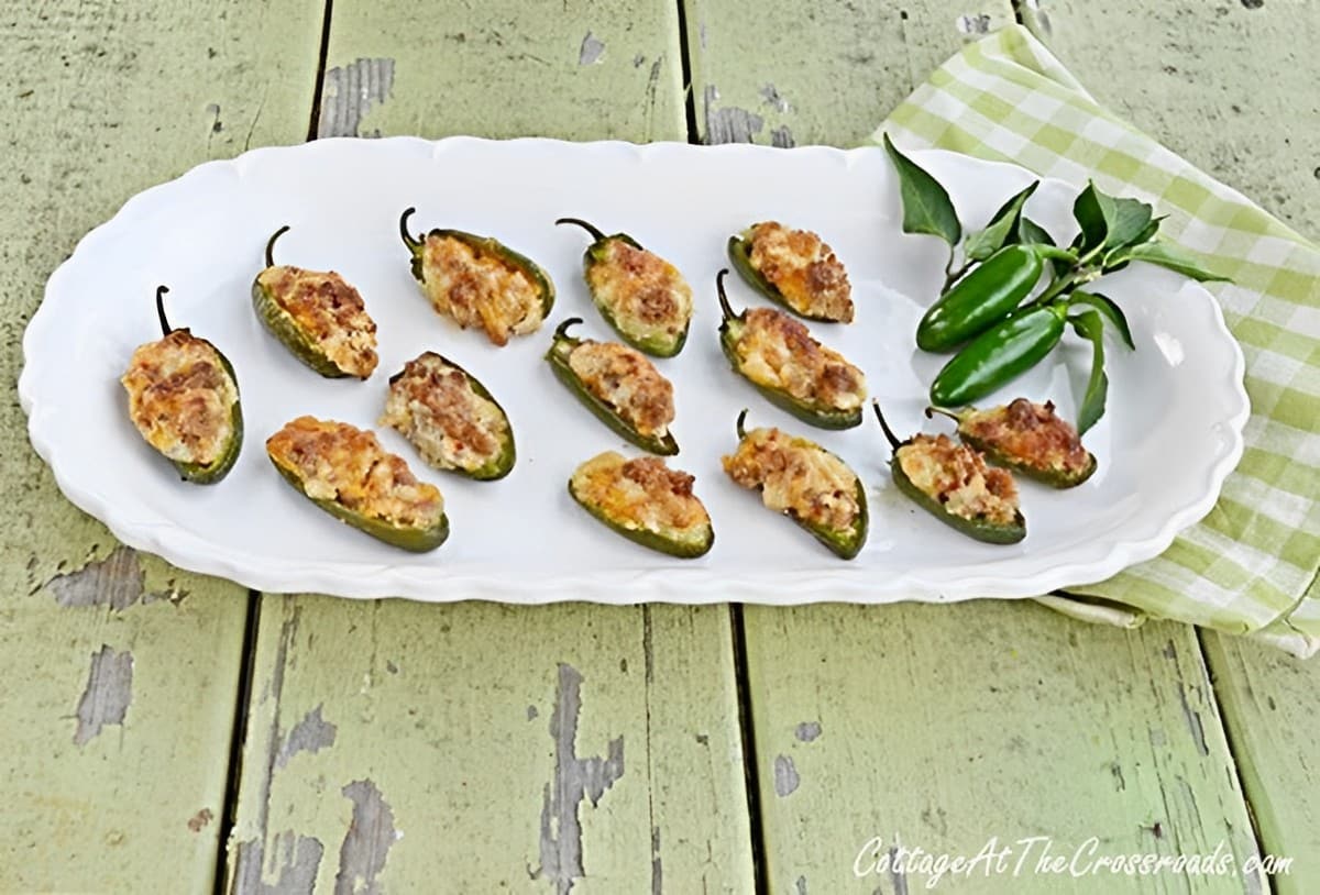 Sausage and cheese stuffed jalapeno peppers on a white tray.