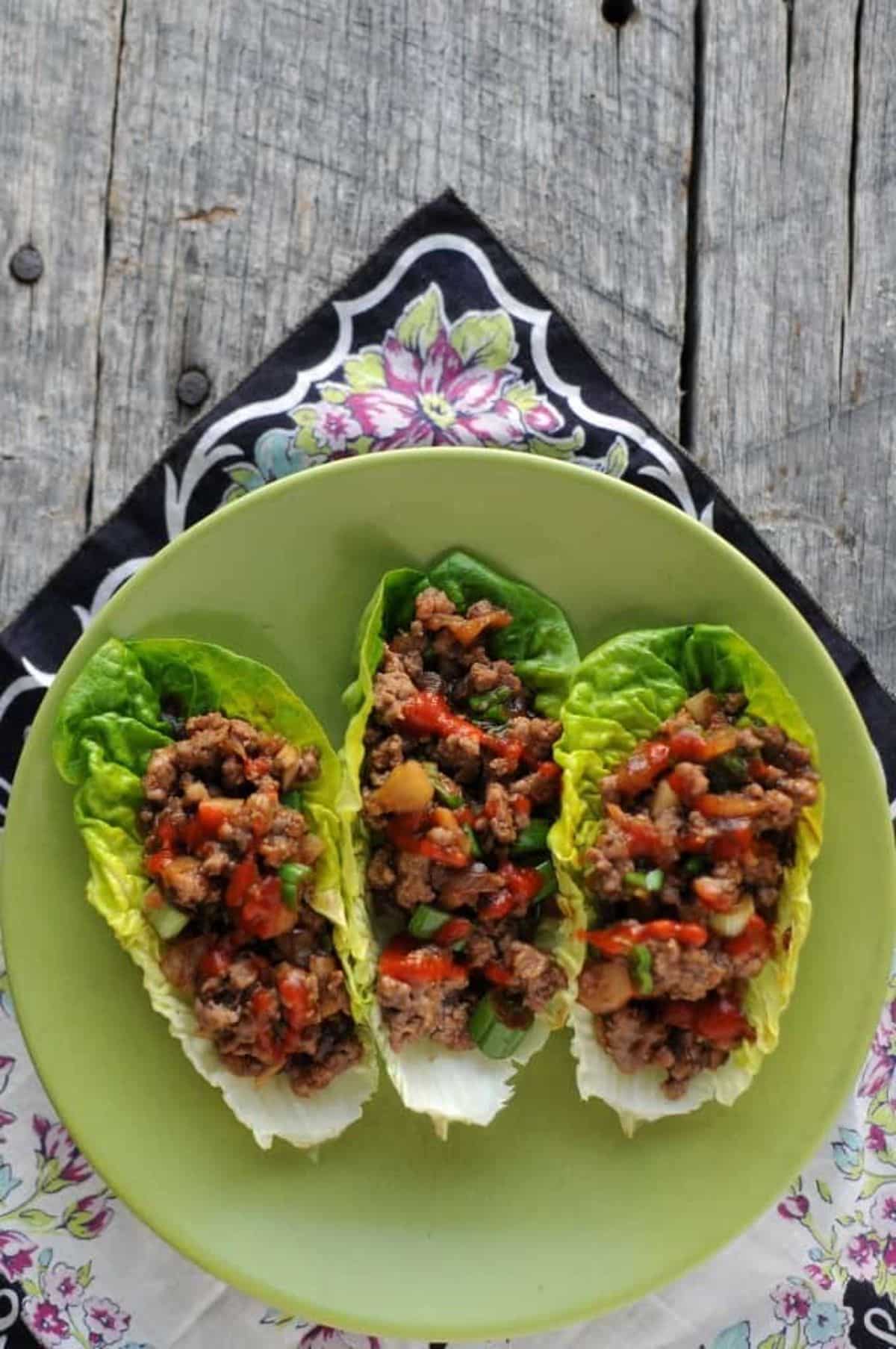 Healthy three ground beef lettuce wraps on a green plate.