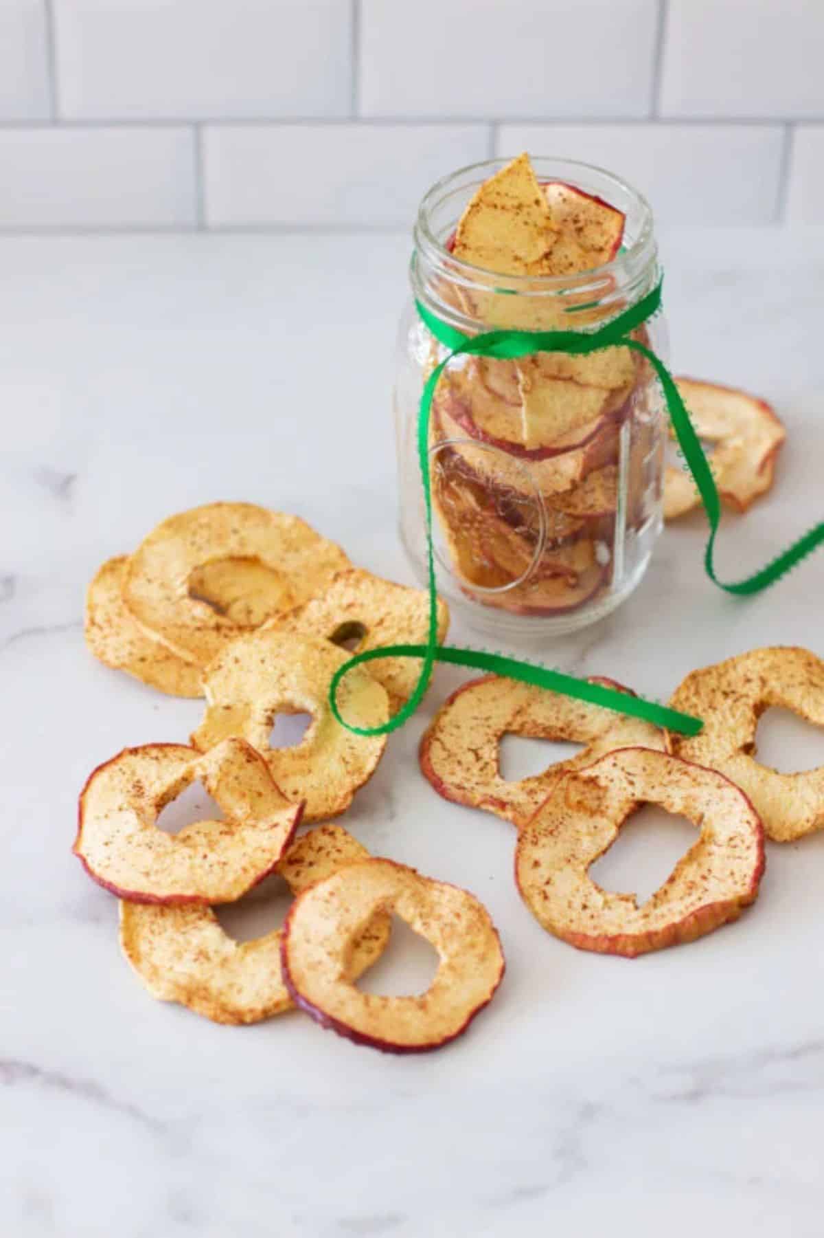 Dehydrated cinnamon apple in a glass jar and scattered on a table.