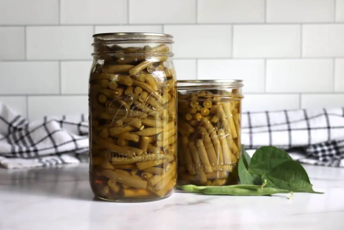 Canned green beans in two glass jars on a countertop.