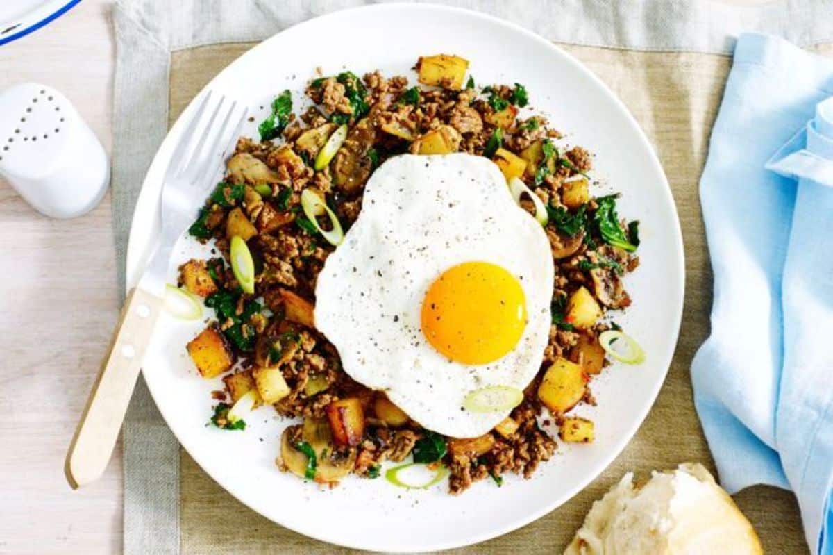 Swede, potato, and beef hash with fried eggs with a fork on a white plate.