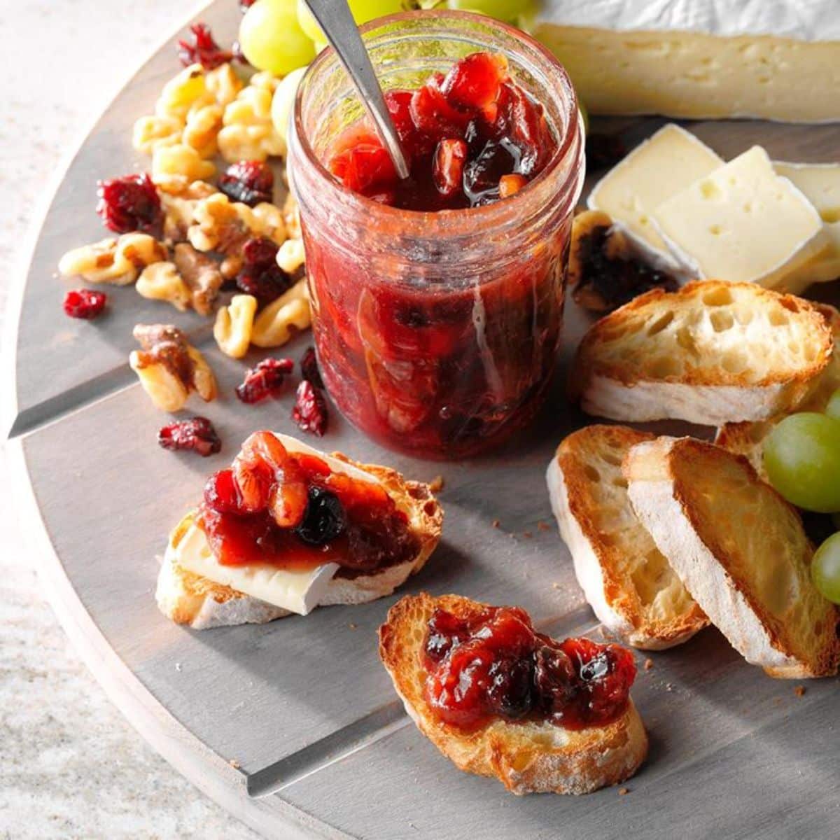 Plum conserve in a glass jar and on pieces of bread on a tray.