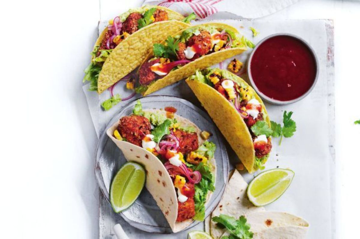 Chicken tacos with grilled corn on a piece of table cloth.