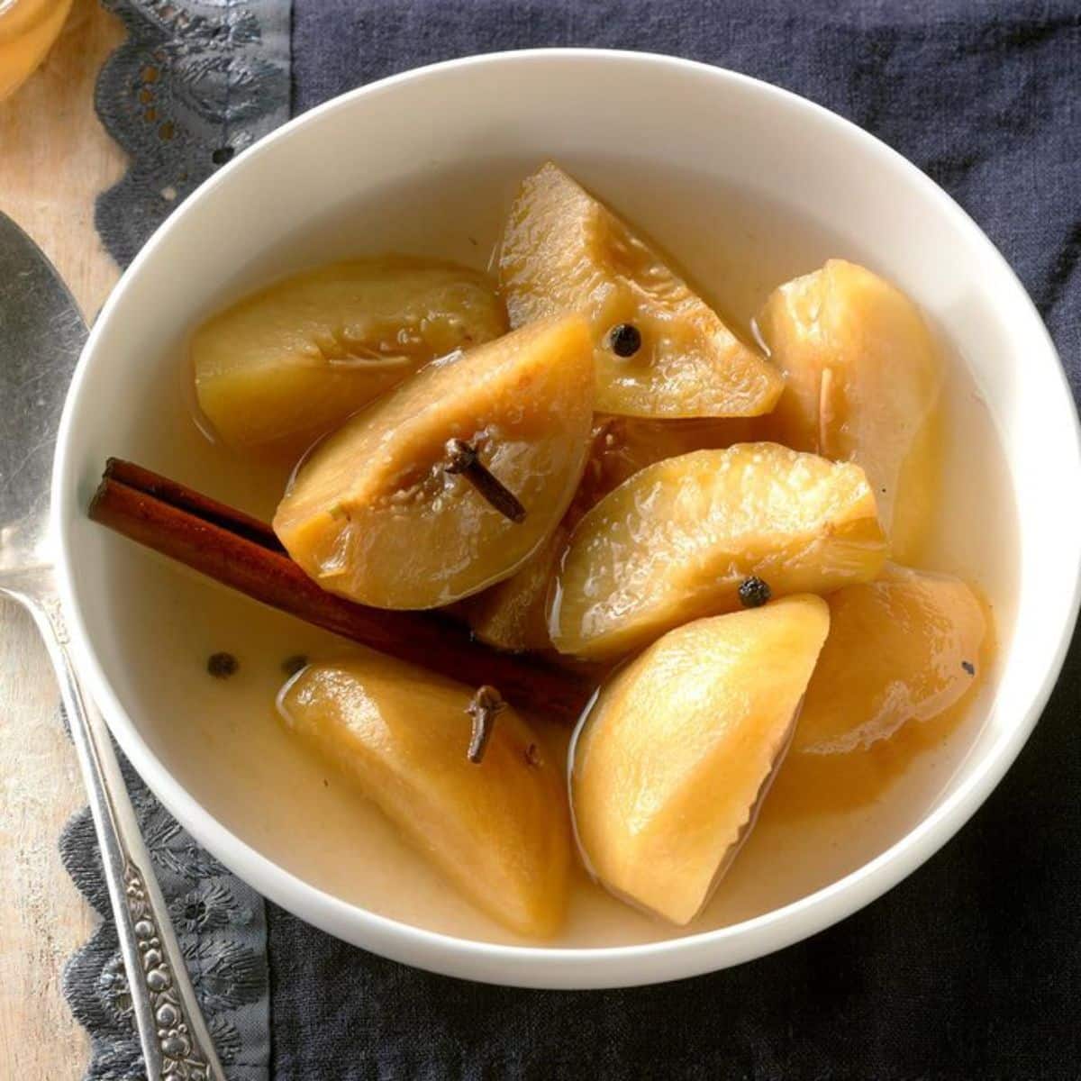 Pickled peaches in a white bowl with a cinnamon stick.
