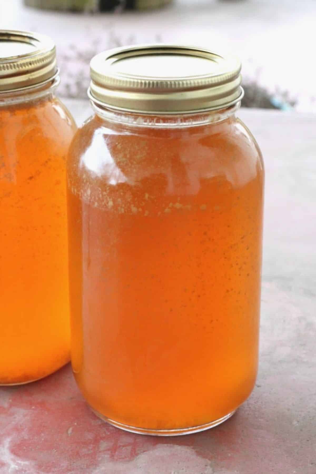 Homemade canned chicken broth in two glass jars.