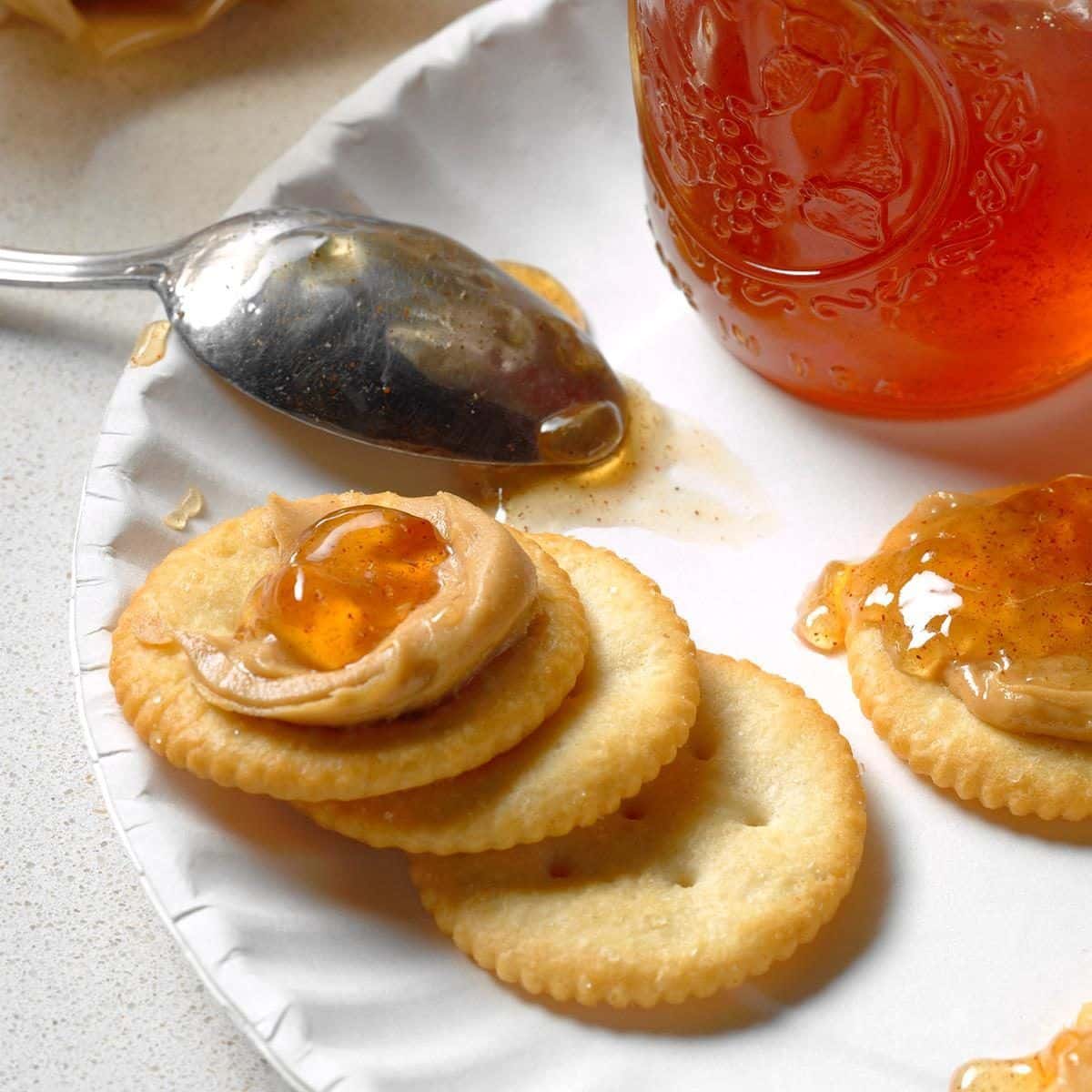 Apple cinnamon jelly in a glass jar and on crackers.