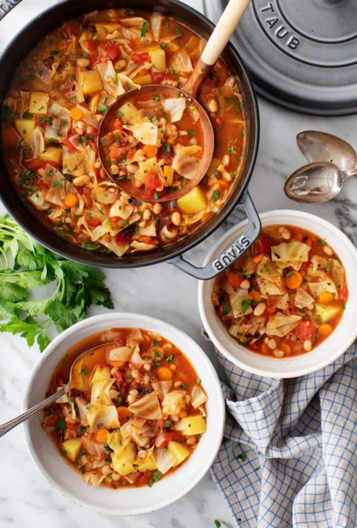 Delicious cabbage soup in a pot and two white bowls.