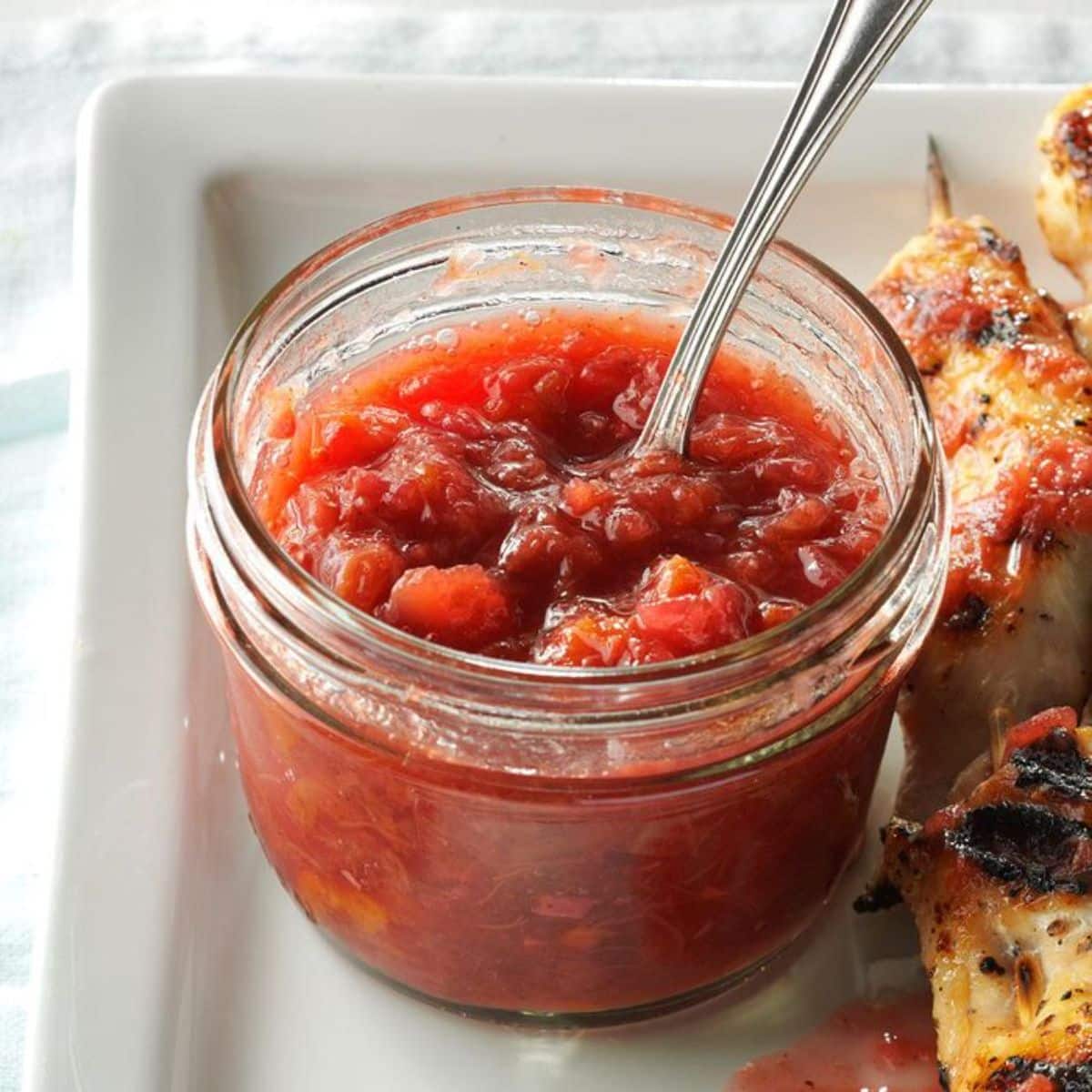 Rhubarb-cherry chutney in a glass jar with a spoon.