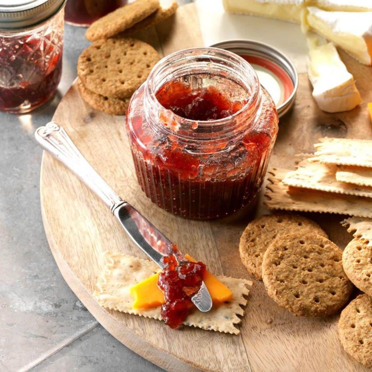 Spiced cranberry, apple, and grape conserve in a glass jar on a wooden tray with crackers.