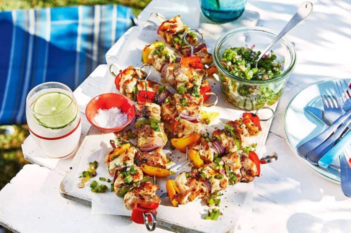 Bbq chicken skewers with green salsa on a white tray.