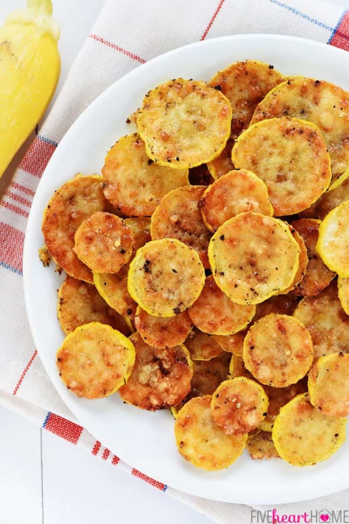 Baked parmesan yellow squash chips on a white plate.