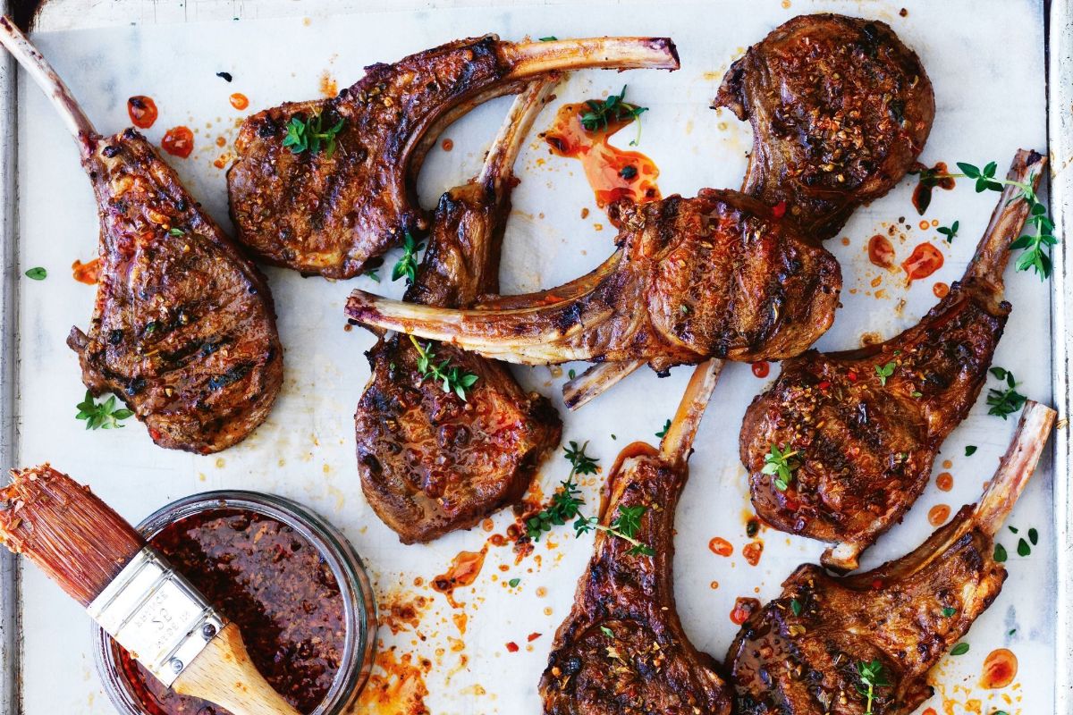 Portuguese-style bbq lamb cutlets on a white tray with a bowl of sauce.