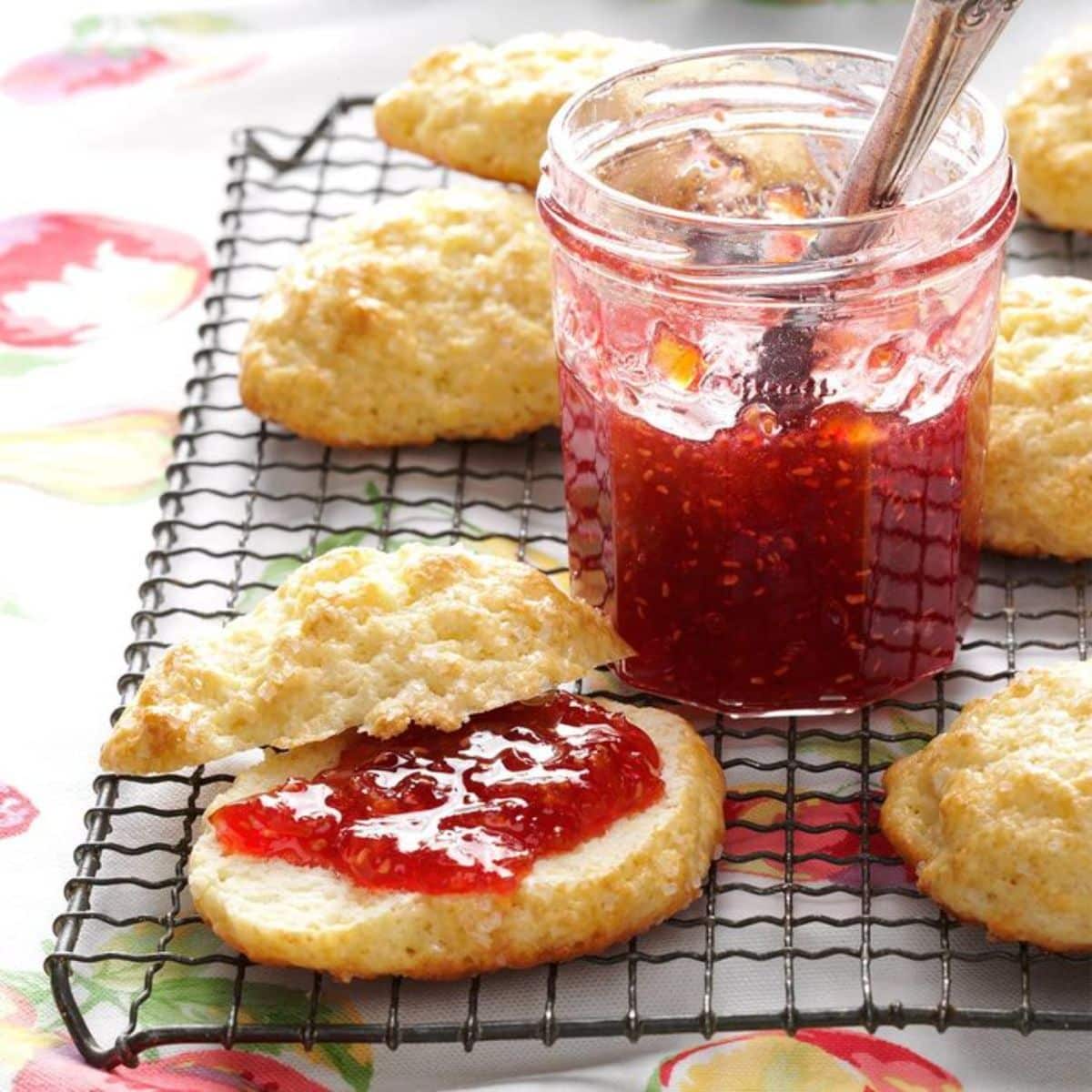Raspberry peach jam in a glass jar and pieces of bread on a resting grid.