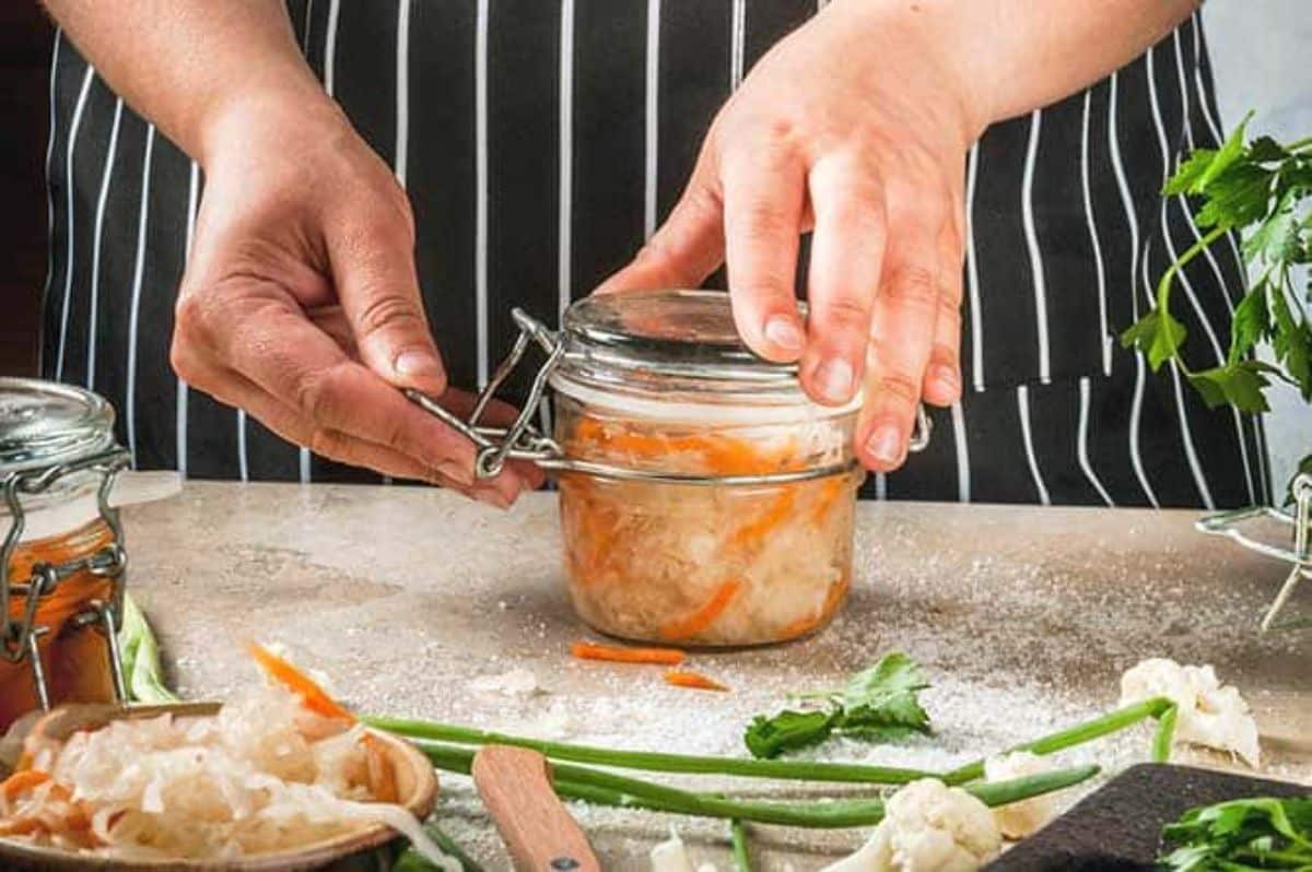 Fermented sauerkraut in a glass jar closed by hands.