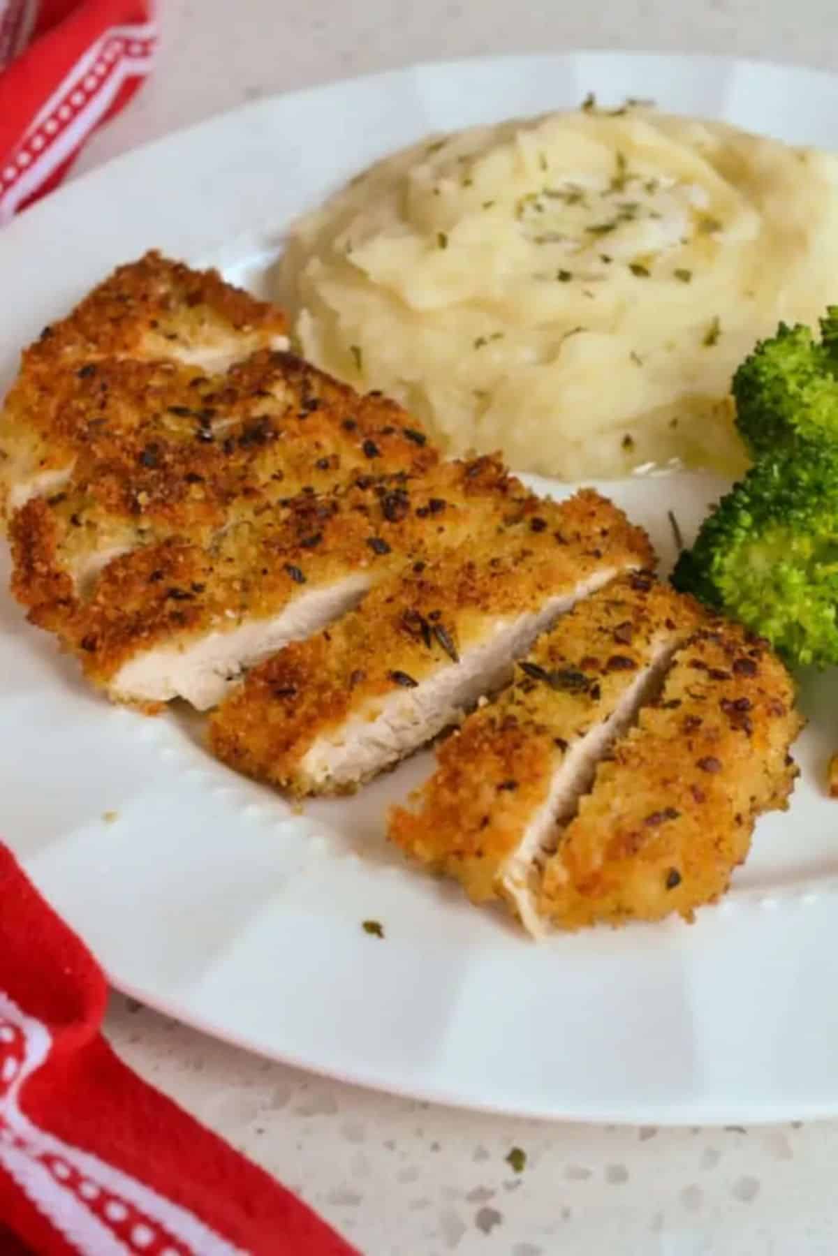 Delicious parmesan crusted chicken with mashed potatoes and broccoli on a white plate.