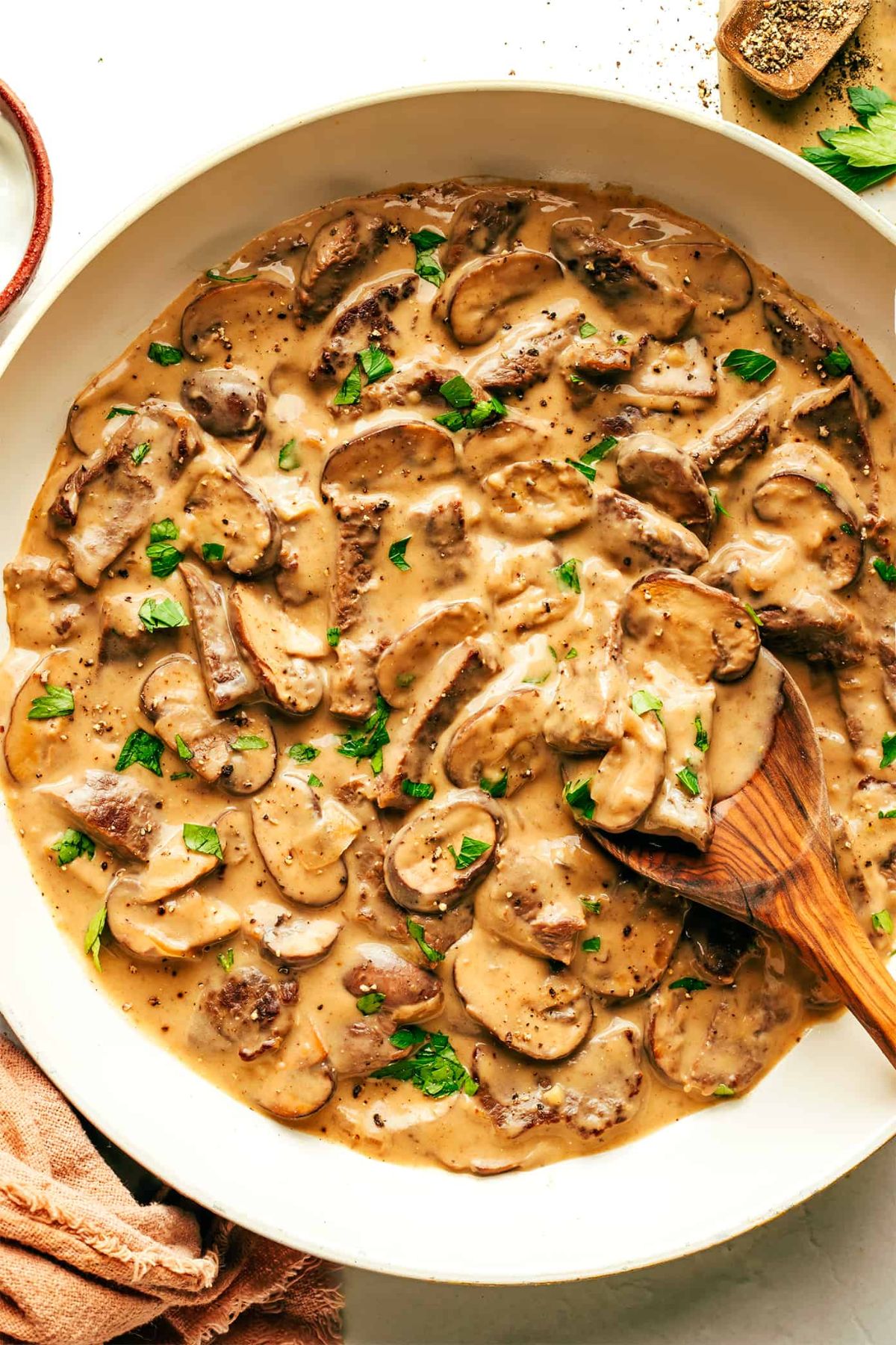 Juicy beef stroganoff in a white bowl with a wooden spoon.