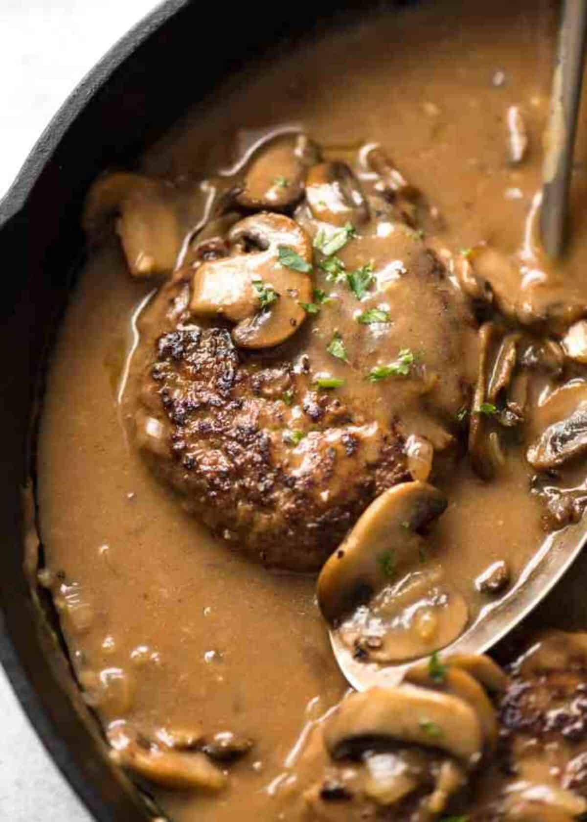 Juicy salisbury steak in a black skillet.