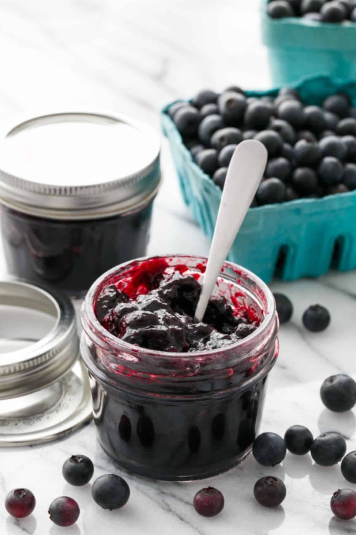 Blueberry vanilla jam in a glass jar with a spoon.