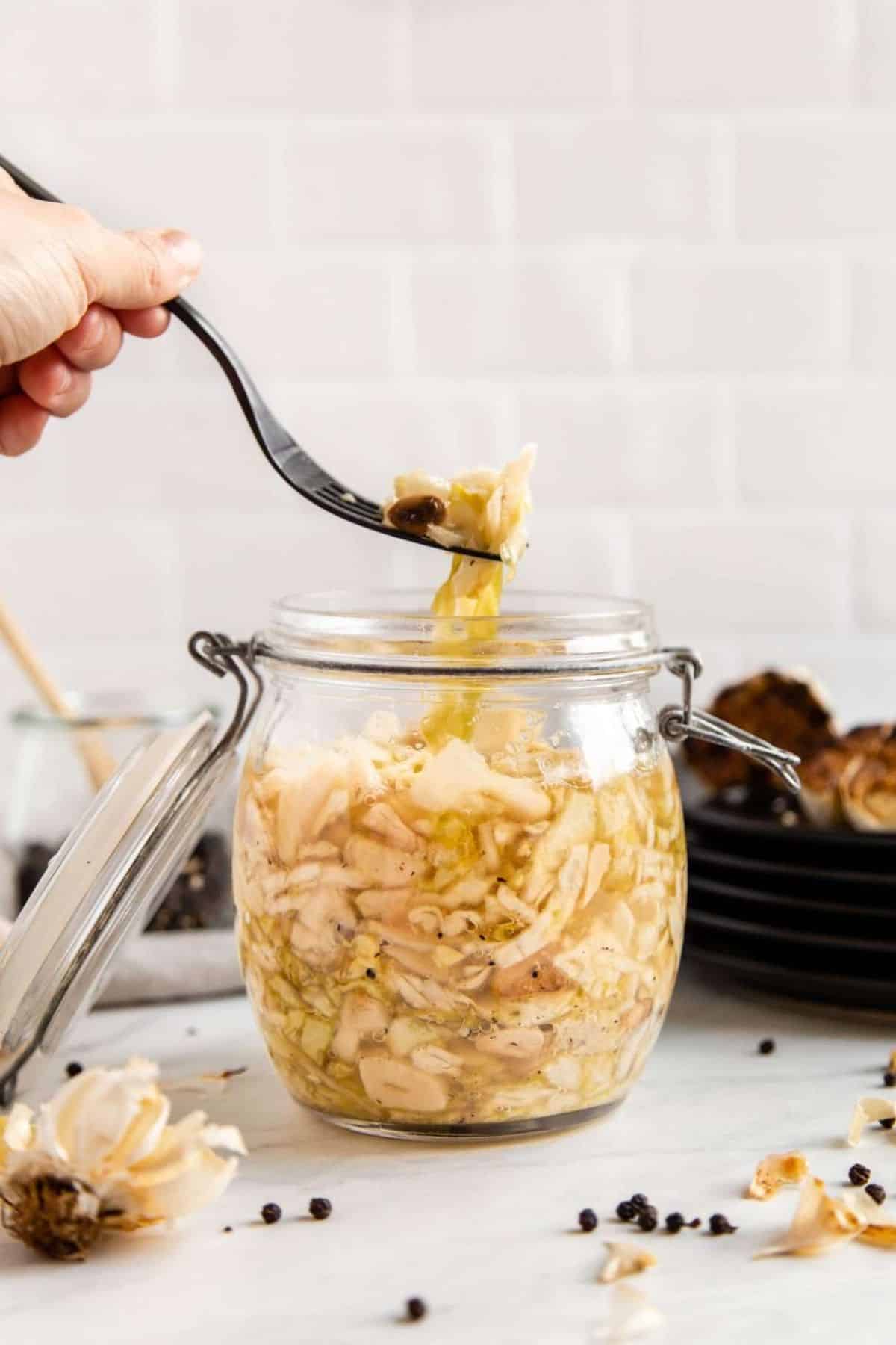 Roasted garlic sauerkraut with black pepper in a glass jar picked with a spoon.