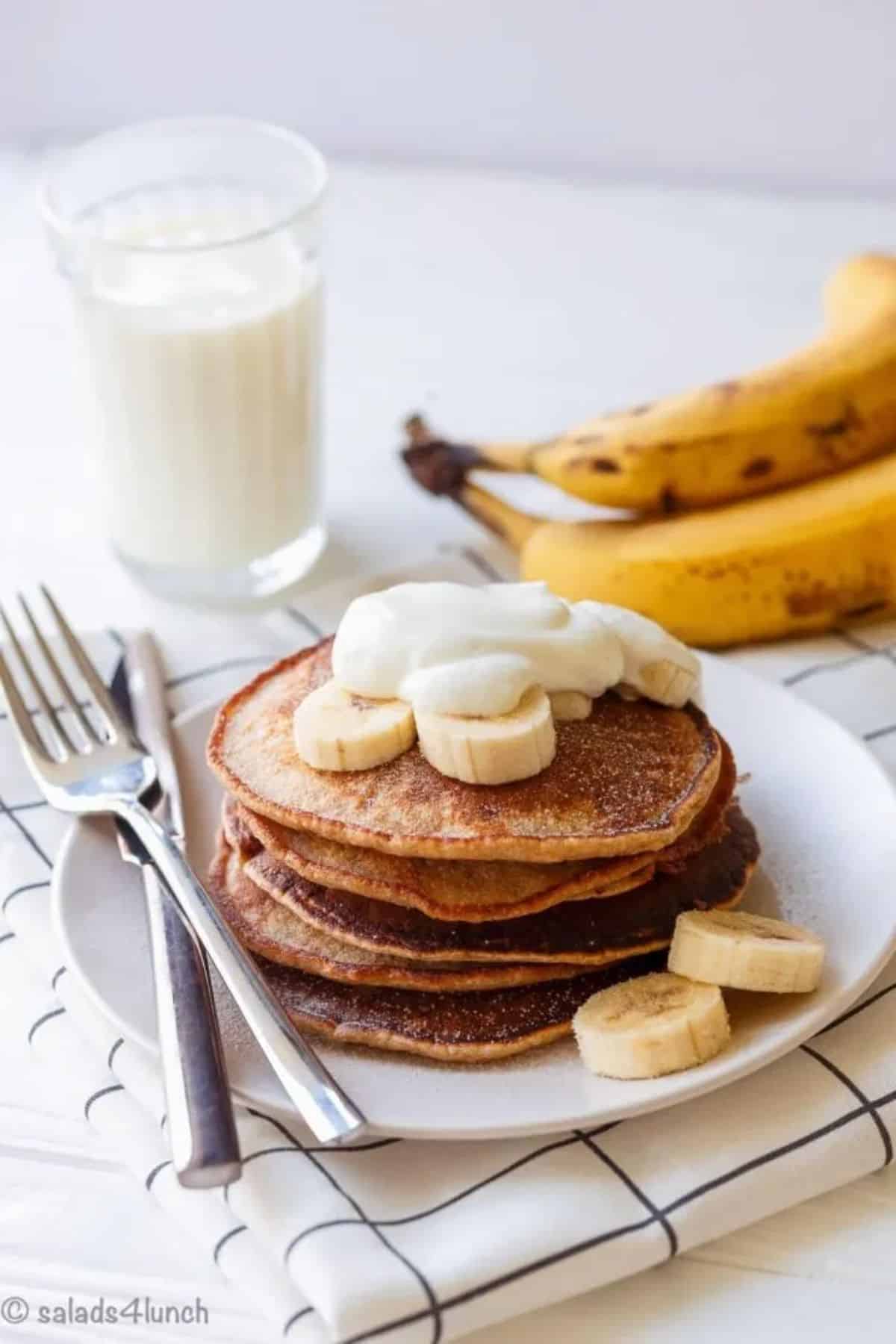 A pile of fluffy, no sugar whole wheat pancakes on a white plate with cutlery.