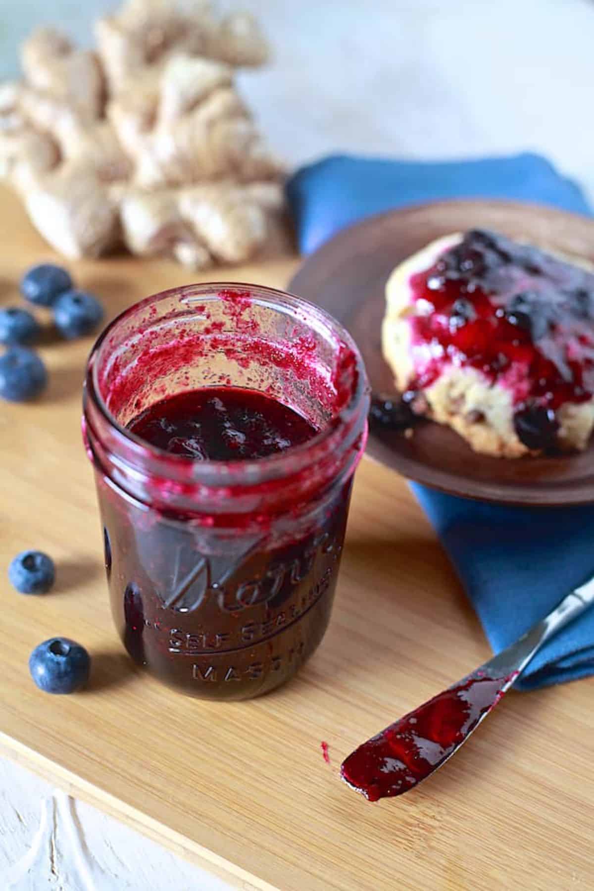 Blueberry ginger jam in a glass jar on a wooden tray.