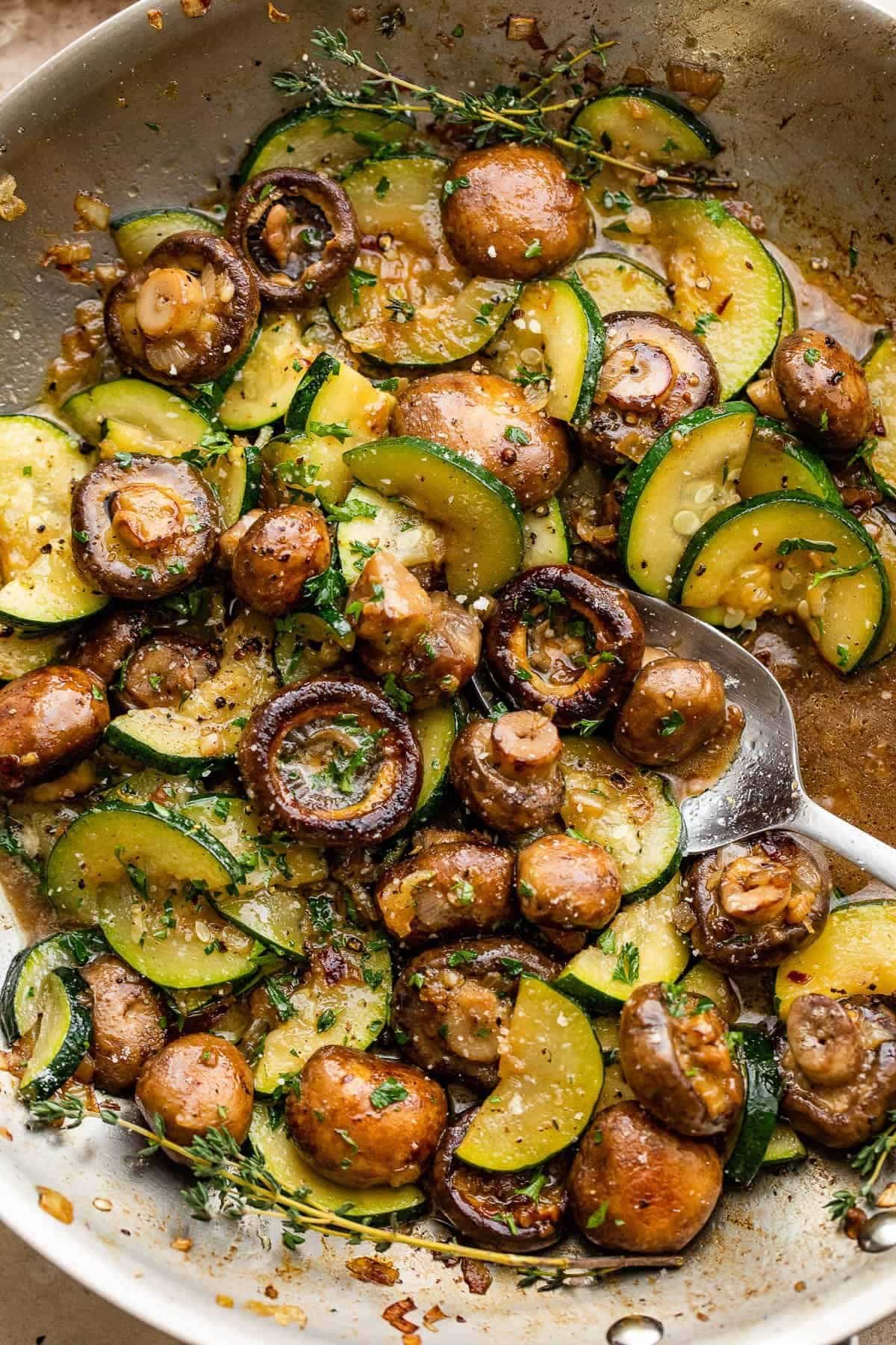 Garlic butter zucchini & mushrooms with a spoon in a skillet.