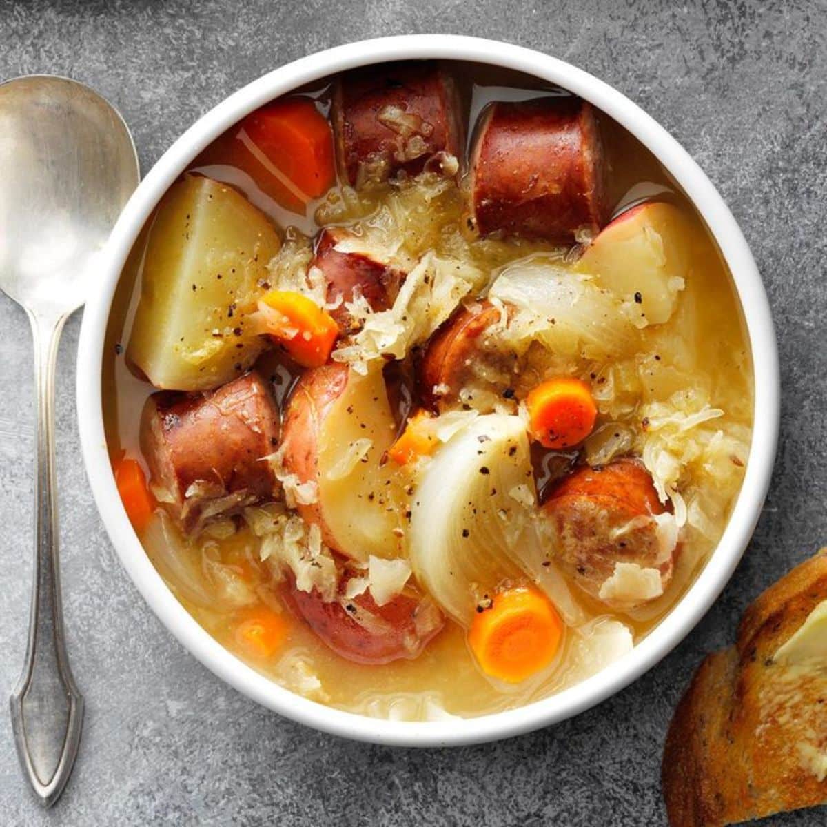 Sausage sauerkraut soup in a white bowl.