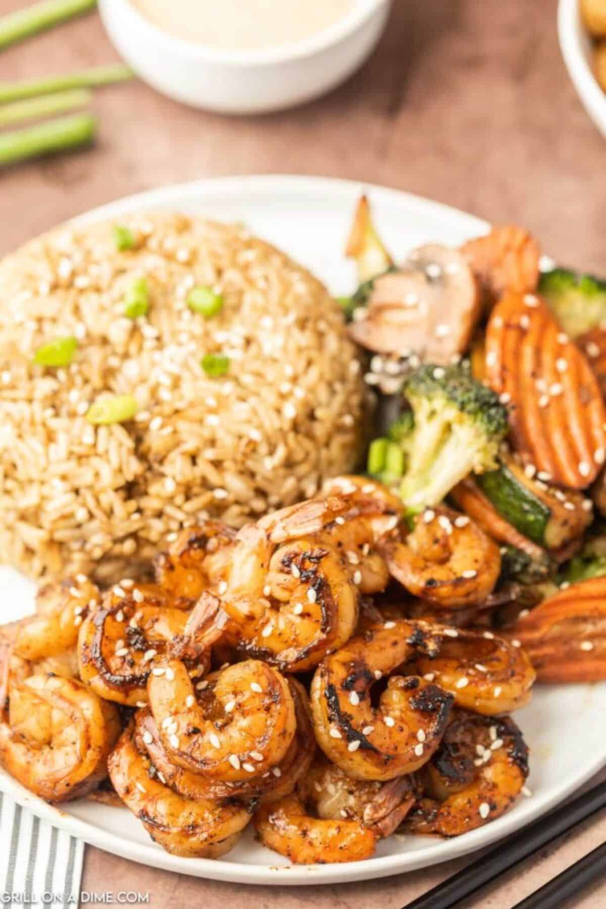 Blackstone hibachi shrimp with veggies and rice on a white plate.