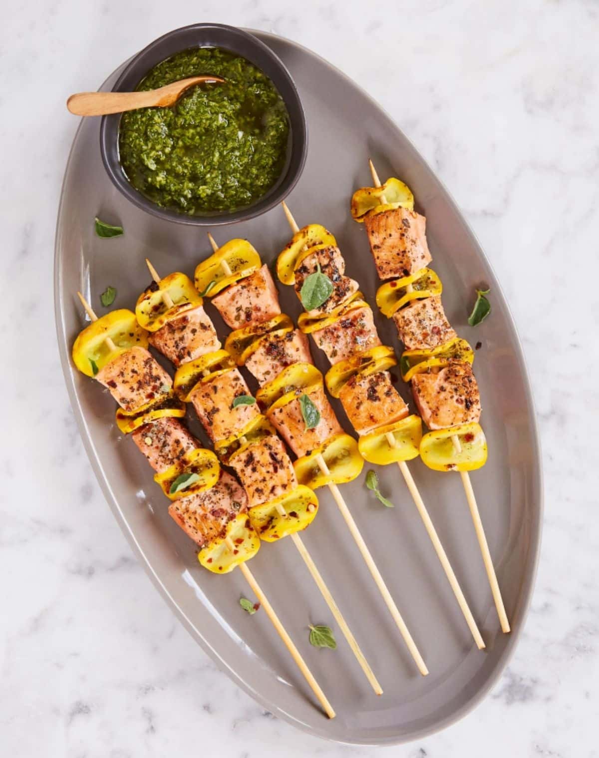 Wild alaska salmon and summer squash kebabs on a gray tray.