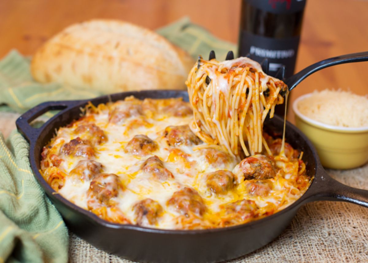 Delicious baked spaghetti & meatballs on a black skillet.