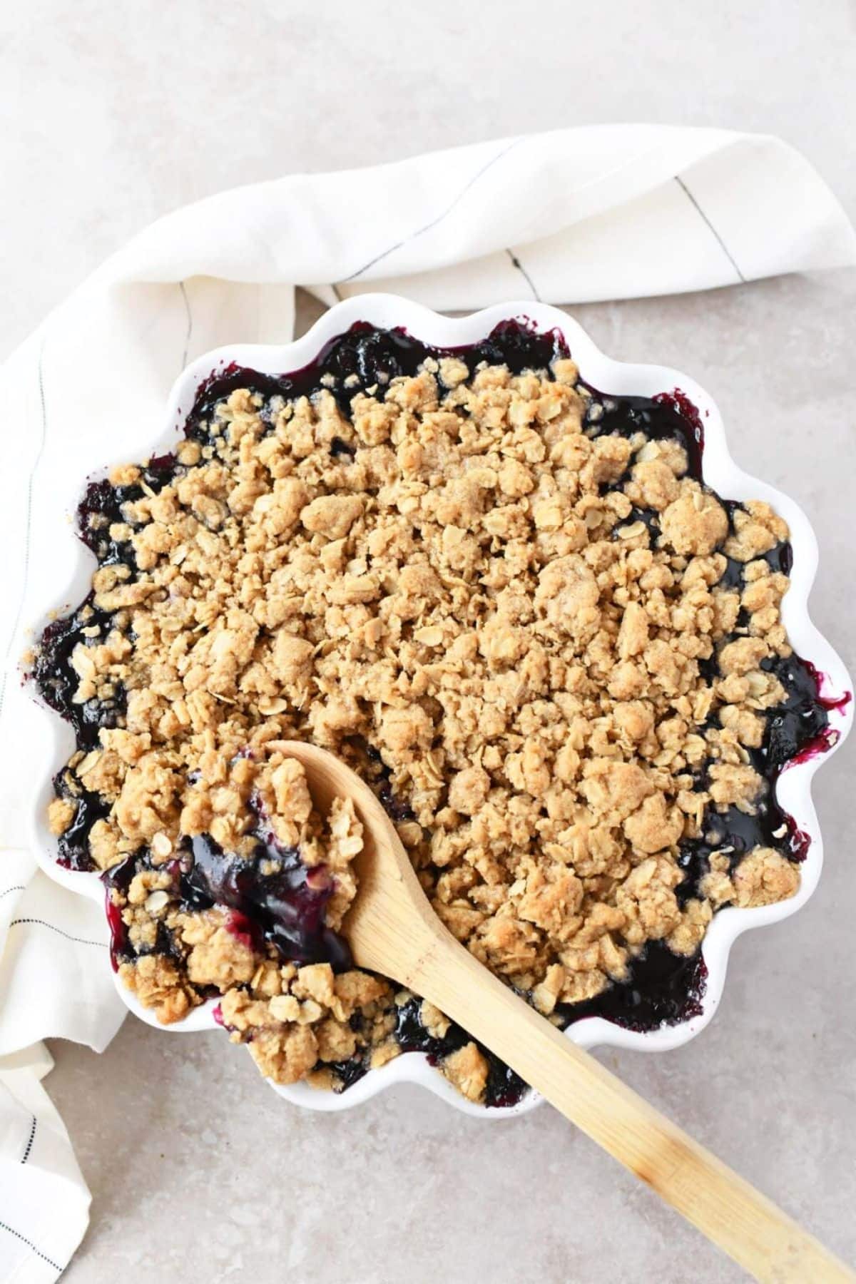 Easy blueberry crisp in a white bowl with a wooden spoon.