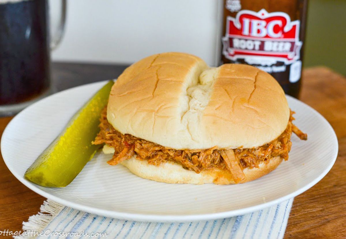 Pulled pork with root beer bbq sauce sandwich with cucumber on a white plate.