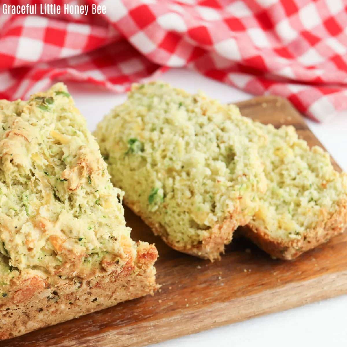 Partially sliced herb and cheddar squash bread on a wooden cutting board.