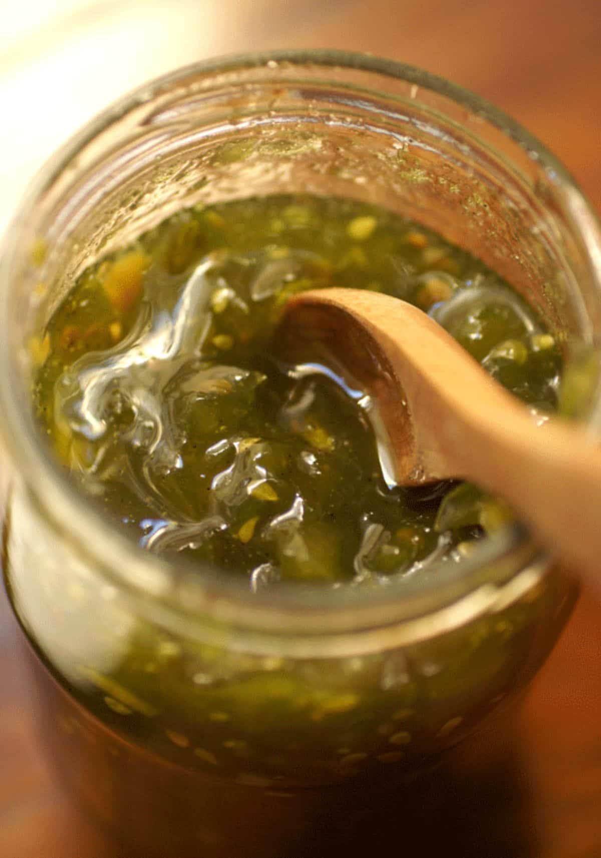 Green tomato jam in a glass jar with a wooden spoon.