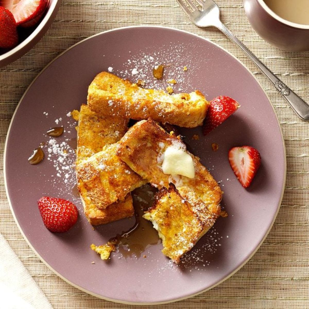 Crispy french toast sticks with strawberries on a pink plate.