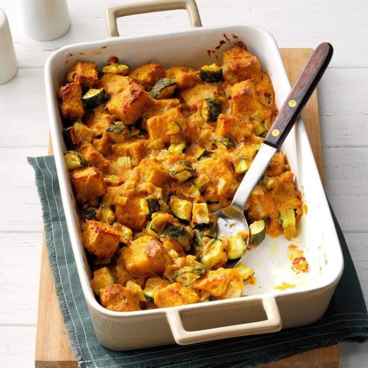 Delicious savory zucchini bread pudding in a white casserole with a spatula.