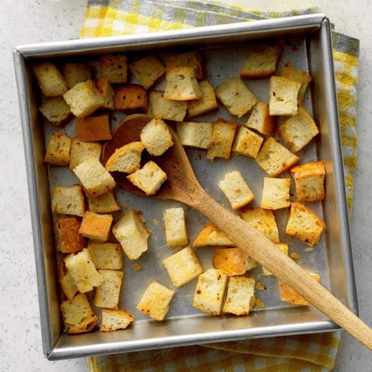 Flavorful croutons in a pot with a wooden spoon.