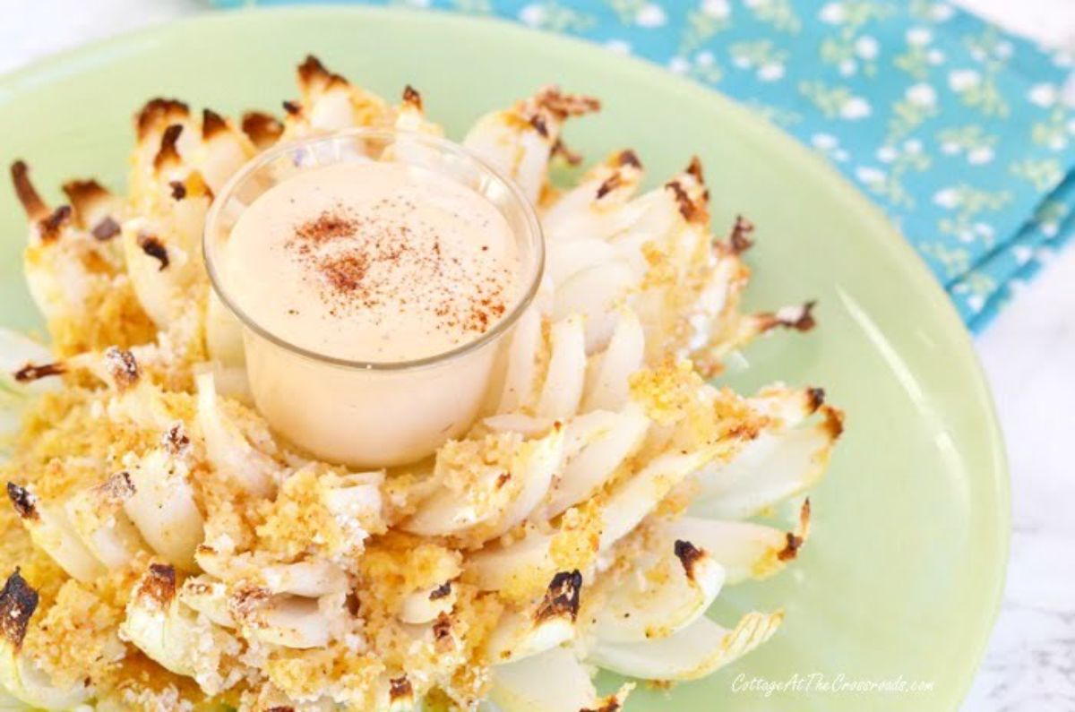 Crispy blooming onion with a bowl of dip on a green plate.