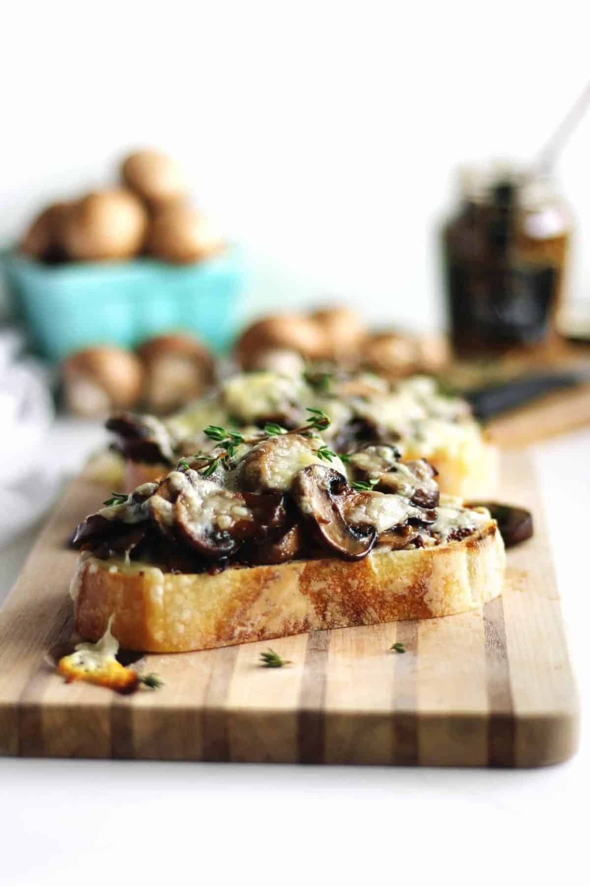 Delicious garlic swiss mushrooms on toast on a wooden cutting board.