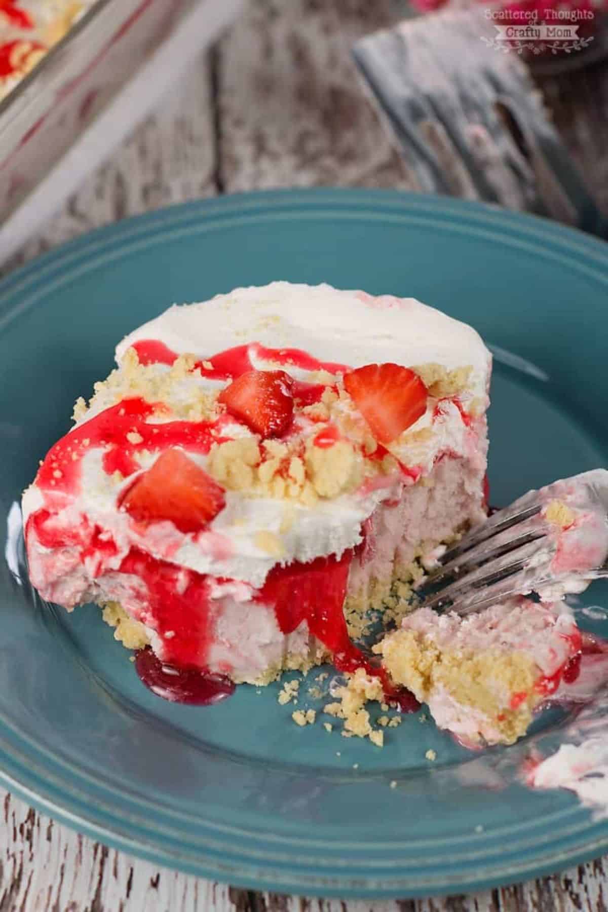 A piece of frozen strawberry ice cream cake on a blue plate with a fork.