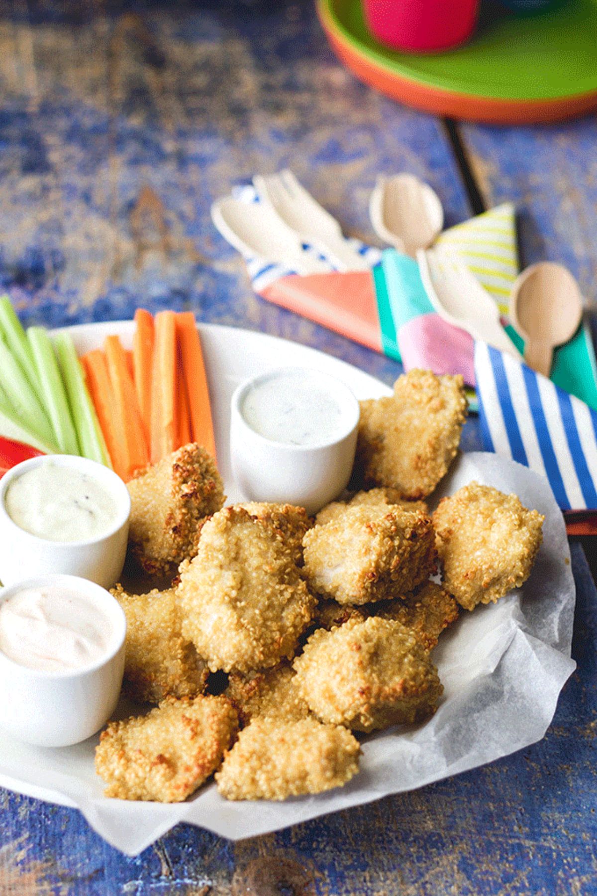 Crispy quinoa-crusted chicken nuggets with bowls of dip and veggies on a white tray.