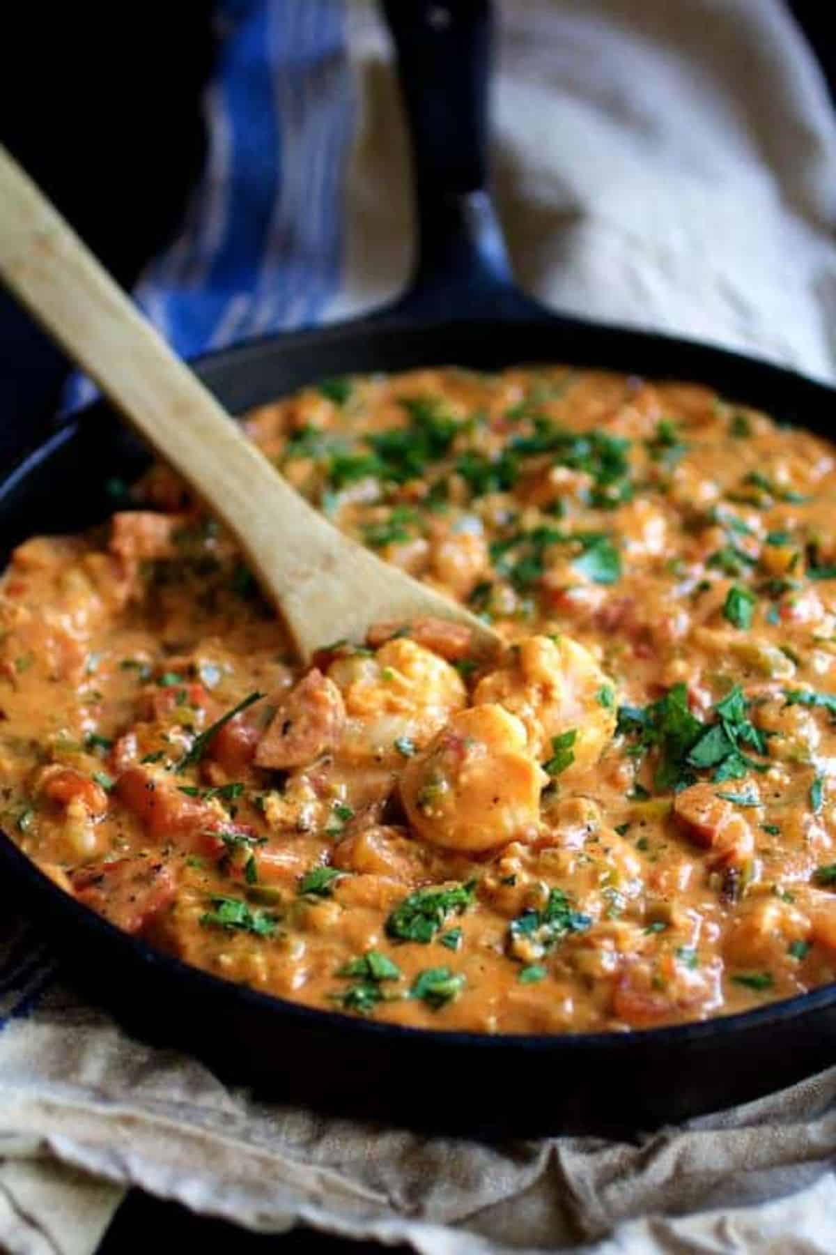 Juicy smothered shrimp and andouille sausage with creamy parmesan peppercorn grits in a skillet with a wooden spoon.